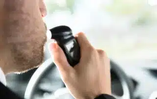 Person seated inside a car using a handheld breathalyzer device, illustrating a 0.05 percent BAC roadside test scenario in Colorado. Image relates to DWAI decision making, showing the moment drivers face choices about contesting a ticket or accepting a plea based on evidence and consequences.