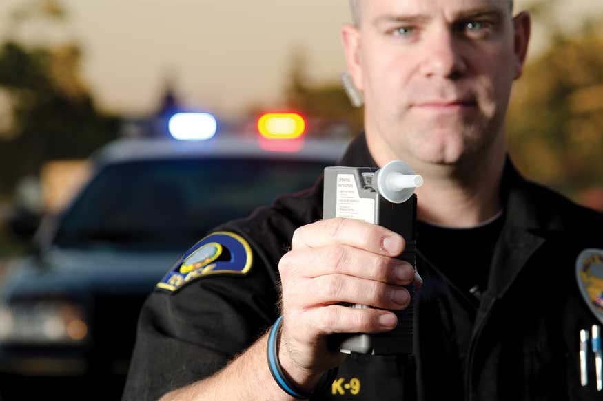 Colorado DUI Breath Test Evidence Police officer holding a breathalyzer in front of car. - Colorado DUI Breath Test Evidence