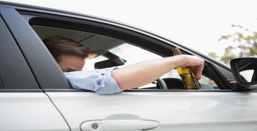 Driver holding beer bottle out car window.