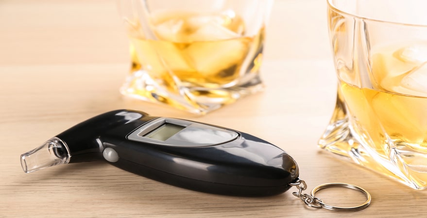 Breathalyzer device with whiskey glasses on table.