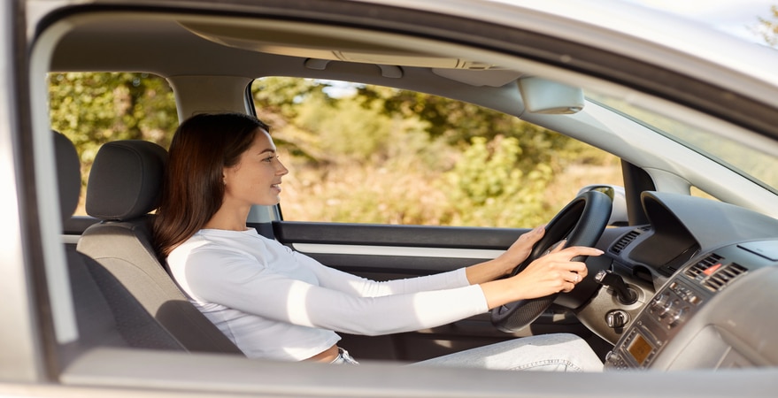 Profile portrait of delighted satisfied beautiful female with glad positive expression, being satisfied with riding car alone, sits on driver`s seat, looking at road with positive expression
