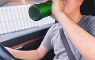 Person drinking from bottle while driving car.